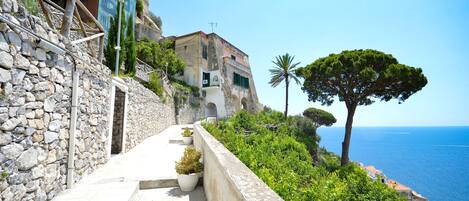 A stone pathway leading to a building with a view of the sea.