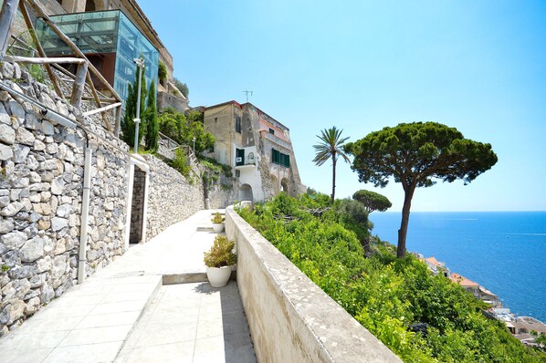 A stone pathway leading to a building with a view of the sea.