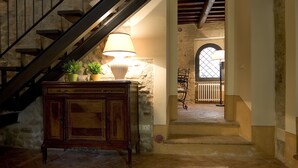 Una escalera con un armario de madera y plantas en macetas, que lleva a una habitación con pared de piedra y una ventana.