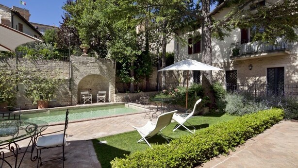 Un patio con piscina, mobiliario exterior y un muro de piedra.