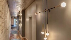 Un pasillo con piso de madera, un tapete azul estampado y una lámpara moderna con varias bombillas.