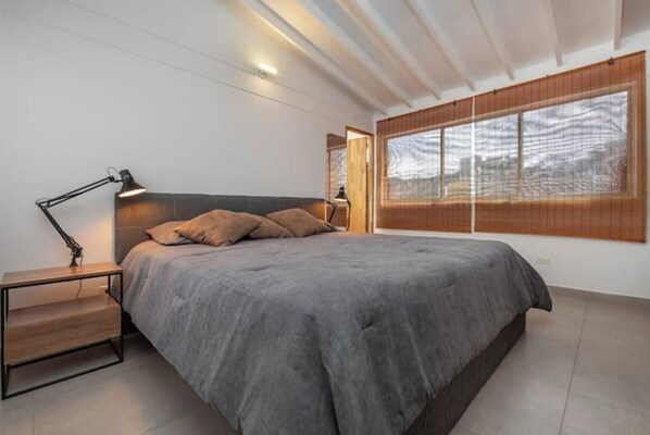 Une chambre moderne avec un grand lit, des lampes de chevet, une table de chevet et une grande fenêtre donnant sur un beau paysage.