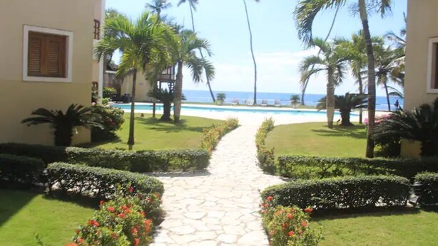 Un sendero conduce a una piscina rodeada de palmeras y setos cuidados.