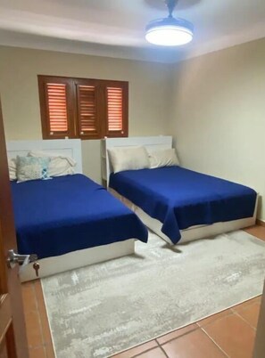 Ein Zimmer mit zwei Betten, einem Deckenventilator und einem Fenster mit Jalousien.