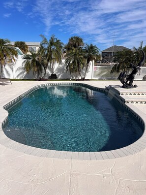 Une piscine d’un bleu éclatant, à bords incurvés, entourée d’une clôture blanche et de palmiers.