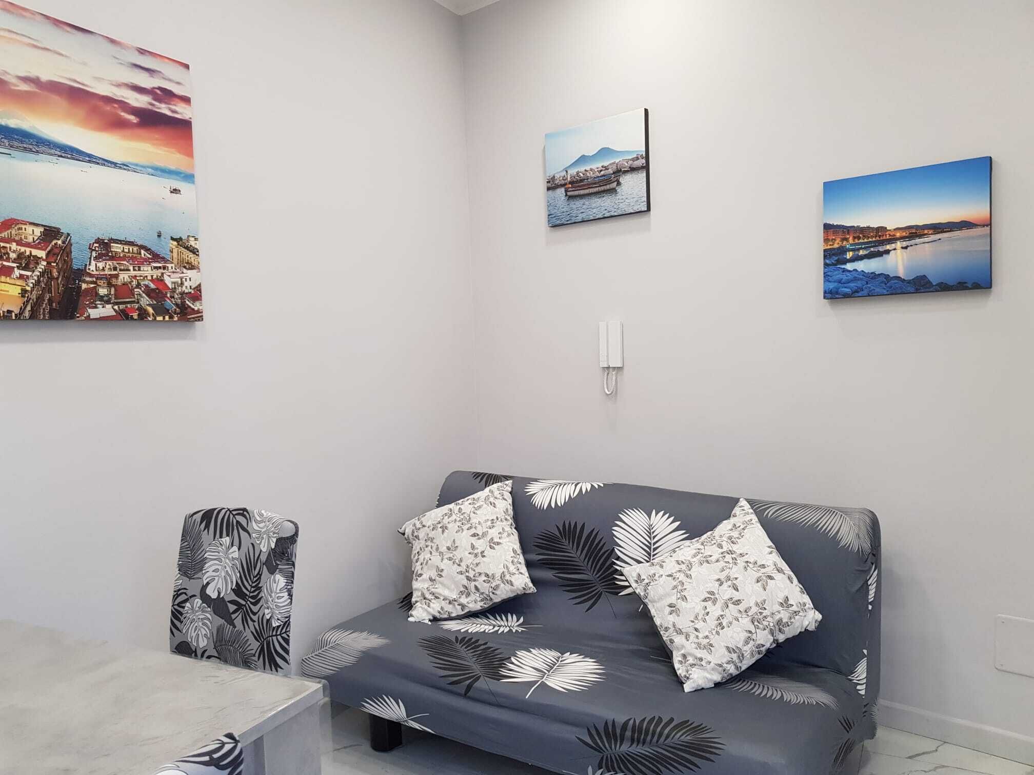 A modern living room with a grey sofa adorned with leaf patterns, a small table, and three framed artworks depicting coastal scenes.