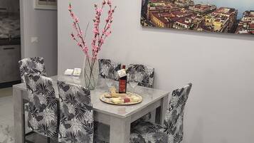 A dining area with a table set for two, featuring a vase with pink flowers, a bottle, and a glass.