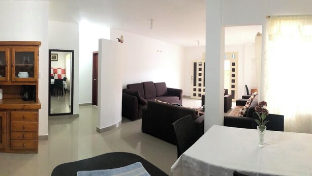 A living room with a wooden cabinet, a sofa, a dining table, and a kitchen area in the background.