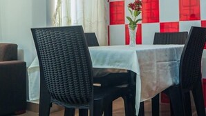 A dining area with a table set for four, chairs, a vase with flowers, and a framed picture on the wall.