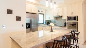 A modern kitchen with stainless steel appliances, a marble countertop, and pendant lighting. - Luxury 3 Bdrm Condo in Playacar. Tennis & Golf Close By, Shops Walking Distance! (Playa del Carmen)
