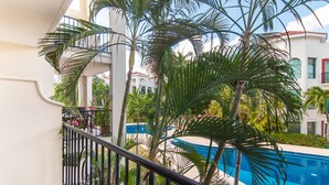 A balcony with a pool view, surrounded by palm trees and a building with balconies. - Luxury 3 Bdrm Condo in Playacar. Tennis & Golf Close By, Shops Walking Distance! (Playa del Carmen)