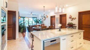 A spacious kitchen with a large island, modern appliances, and a dining area with a ceiling fan. - Luxury 3 Bdrm Condo in Playacar. Tennis & Golf Close By, Shops Walking Distance! (Playa del Carmen)