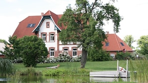 Ein großes, zweistöckiges Haus mit rotem Ziegeldach, einem Teich und einem Steg.