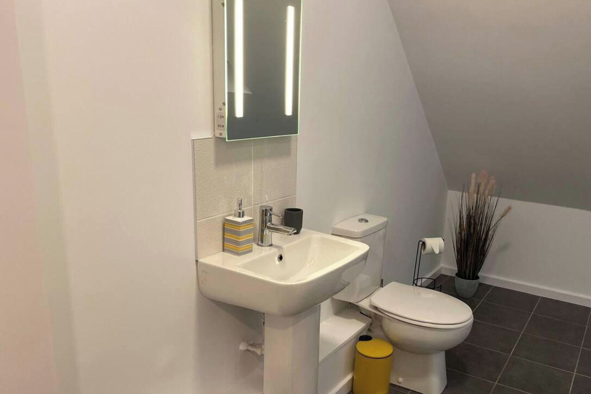 A small, modern bathroom with a white sink, mirror, and toilet.