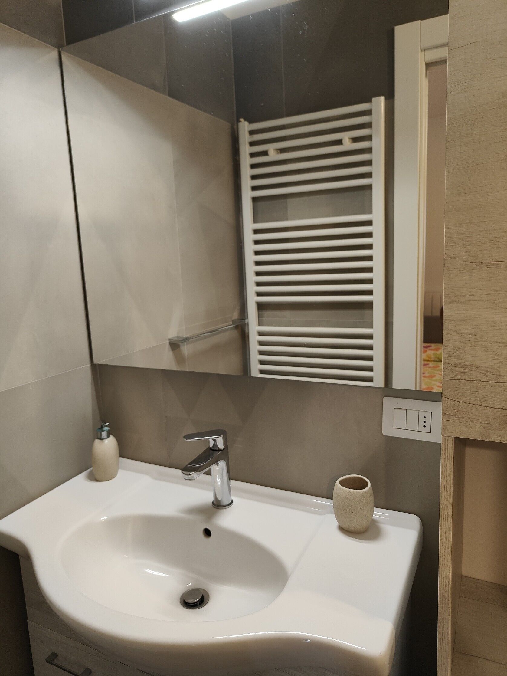 A bathroom with a white sink, a mirror, a towel rack, and a soap dispenser.