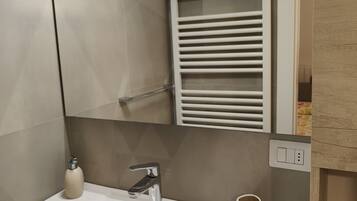 A bathroom with a white sink, a mirror, a towel rack, and a soap dispenser.