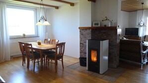 A dining area with a wooden table and chairs, a fireplace, and a television in a modern living space. - Vacation cottage Ferber (Wiesbaum)