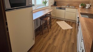 A modern kitchen with a built-in microwave, wooden stools, a window with a view, and a sink. - Vacation cottage Ferber (Wiesbaum)