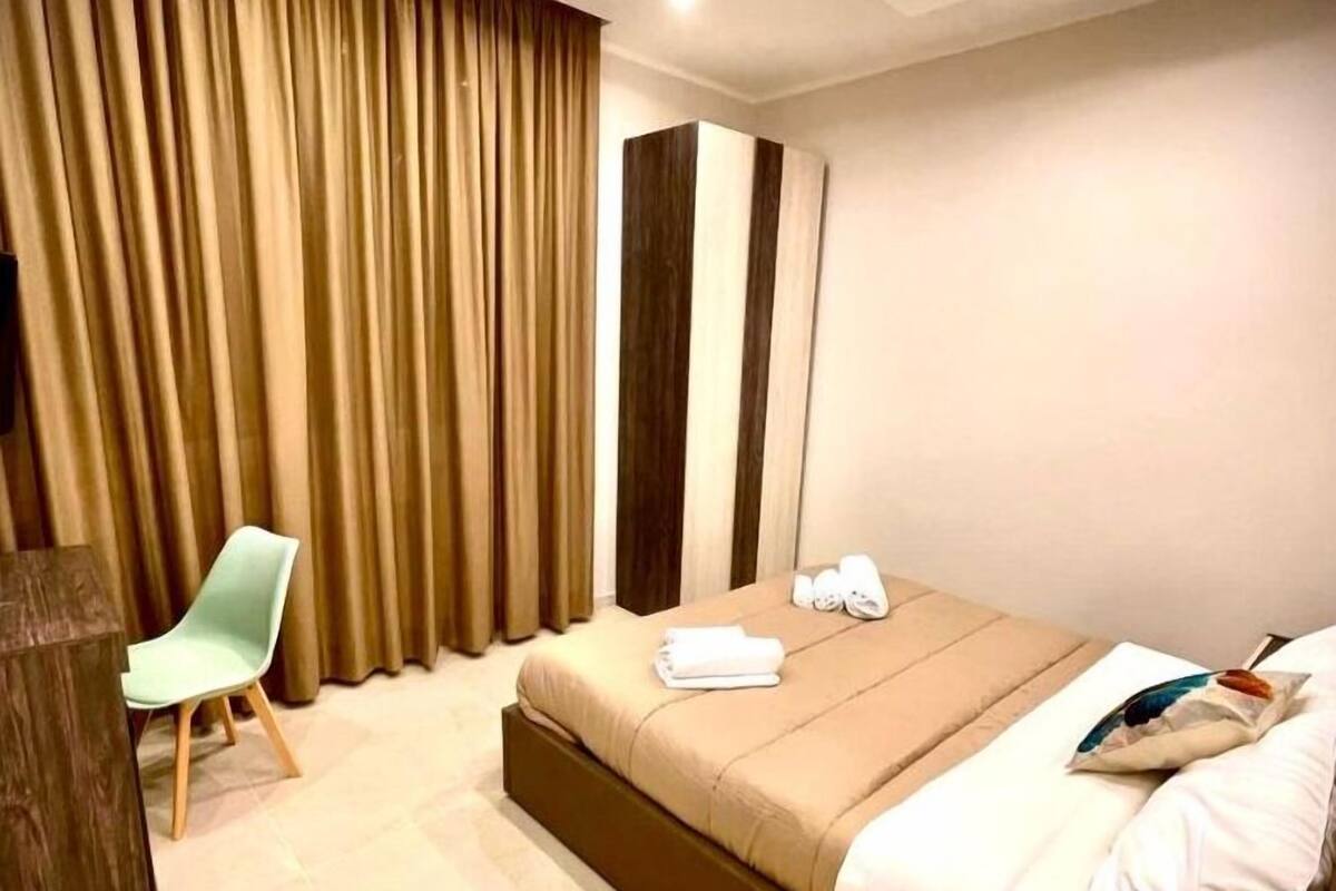 Ett modernt hotellrum med en säng, en stol och ett stort fönster med gardiner.