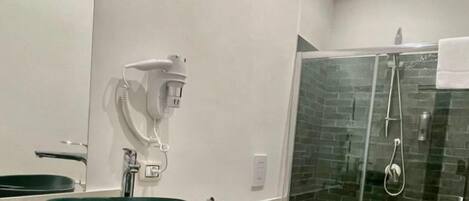 A modern bathroom with a green vessel sink, a glass shower enclosure, and a bidet.