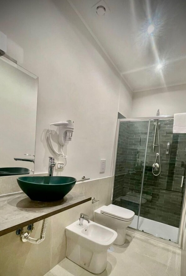 A modern bathroom with a green vessel sink, a glass shower enclosure, and a bidet.