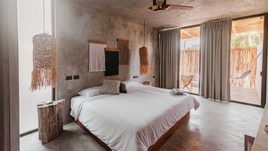 Een ruime slaapkamer met een groot bed, een plafondventilator, uitzicht op de omgeving en een hangmat buiten het raam.