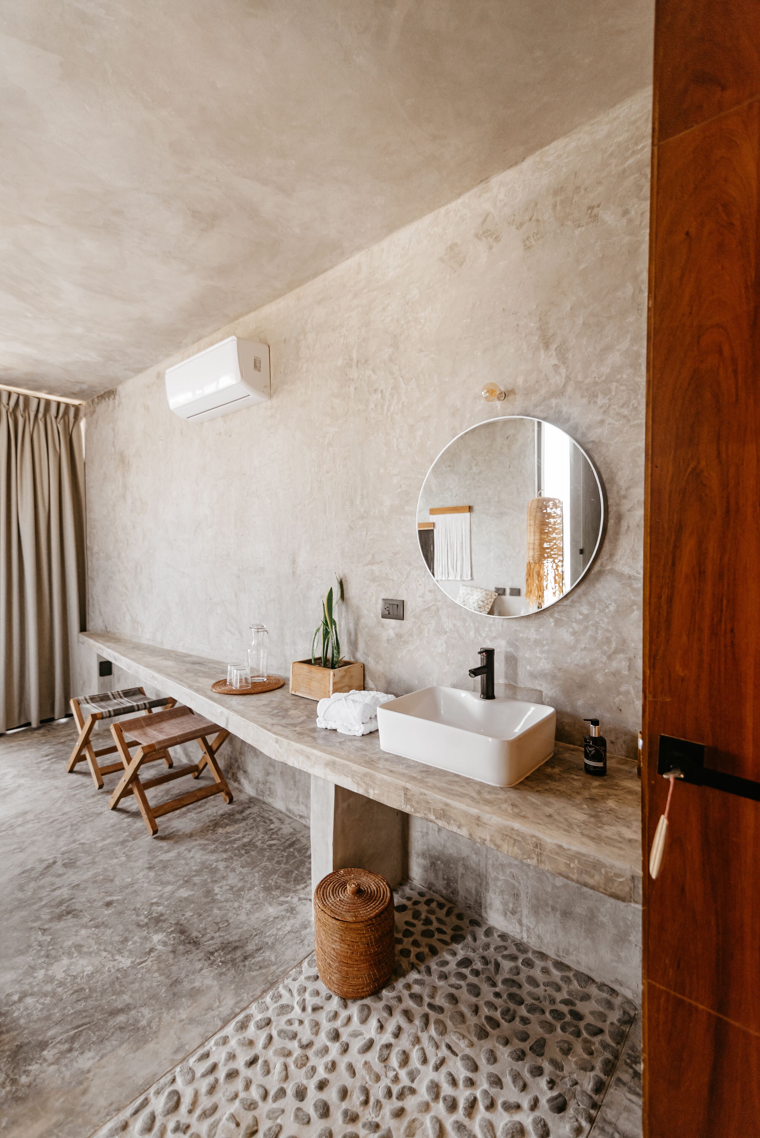 A bathroom with a large mirror, two sinks, a wooden stool, and a textured floor.