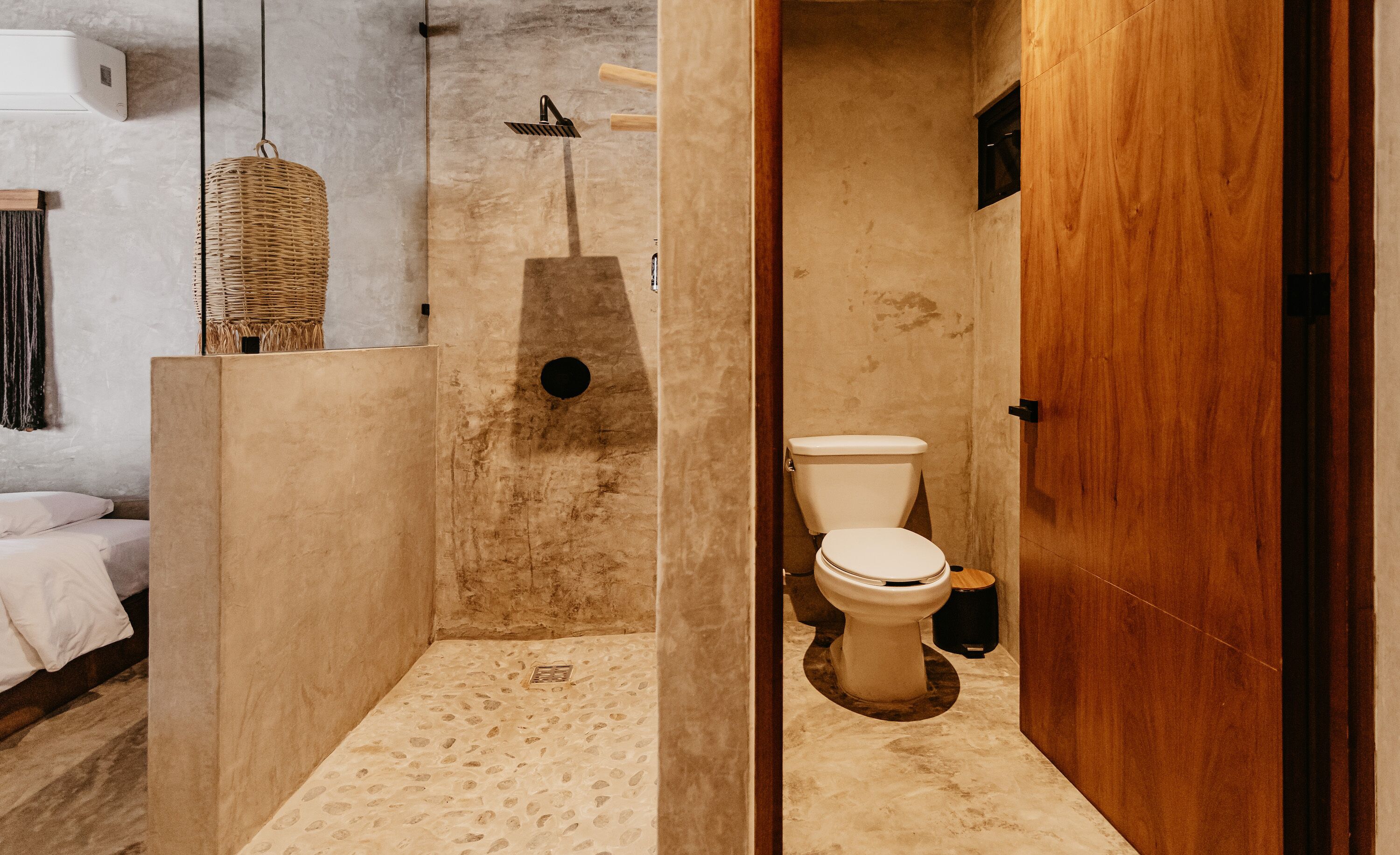 Een badkamer met douche en toilet, en een bed in de aangrenzende kamer.