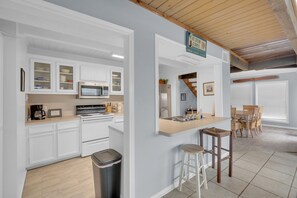 A kitchen with white cabinets, a microwave, and a stove. There is a trash can and a bar area with stools.