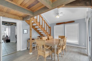 A dining area with a wooden table and chairs, a staircase, and a ceiling fan.