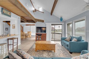 A spacious living area with a wooden coffee table, a blue sofa, a TV, and a kitchen area with a wooden countertop and bar stools.