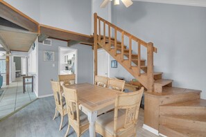 A dining area with a wooden staircase, a dining table with chairs, and a kitchen in the background. - Gated community with POOL on the beach (Matagorda)