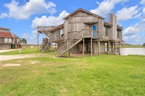 A large wooden house with multiple levels, a staircase, and a dock extending into a body of water.