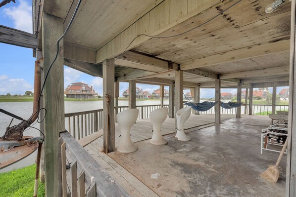 A covered outdoor area with a concrete floor, wooden beams, and a view of houses across a body of water.