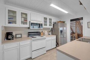 Een keuken met witte kastjes, een magnetron, een fornuis en een koelkast.