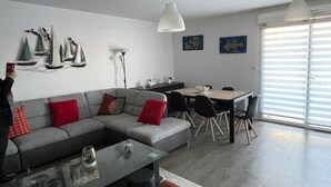 Un salon moderne avec un canapé d’angle gris, une table basse et un coin repas comprenant une table et des chaises en bois.