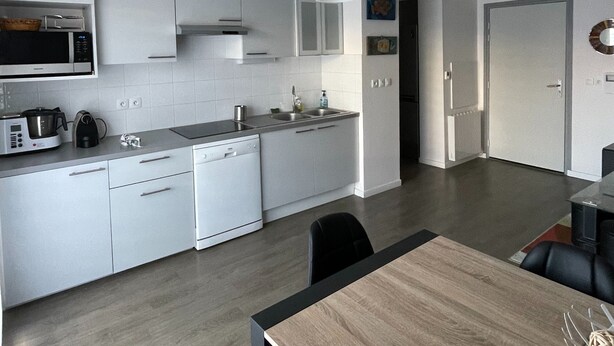Une cuisine moderne avec des meubles blancs, un four à micro-ondes et une machine à café. On y trouve également un coin repas avec une table et des chaises en bois.