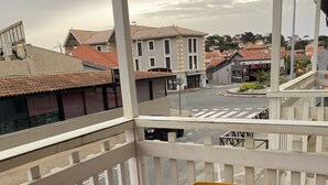 Un balcon avec une table et deux chaises, donnant sur une rue bordée d’immeubles et traversée par un rond-point.