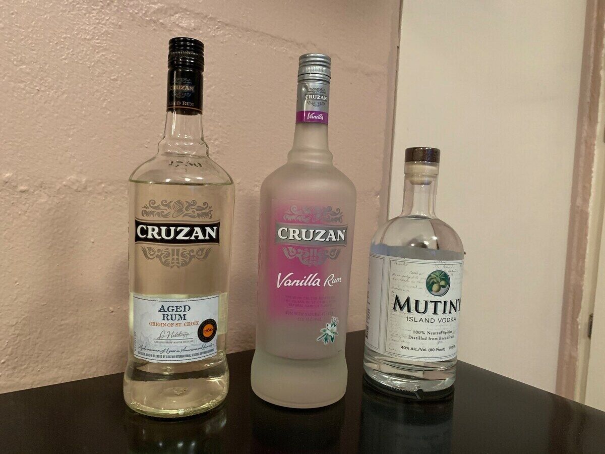 Tre bottiglie di rum Cruzan, una di rum Cruzan alla vaniglia e una bottiglia di vodka Mutiny Island su un tavolo.