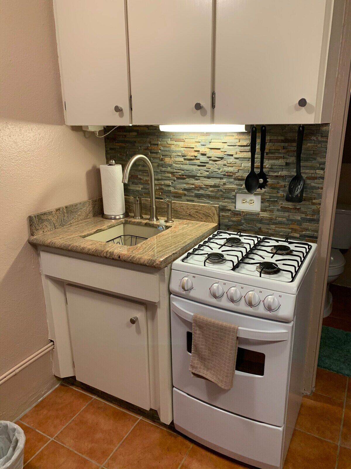 Uma cozinha compacta com fogão a gás, pia e painel de fundo em pedra.