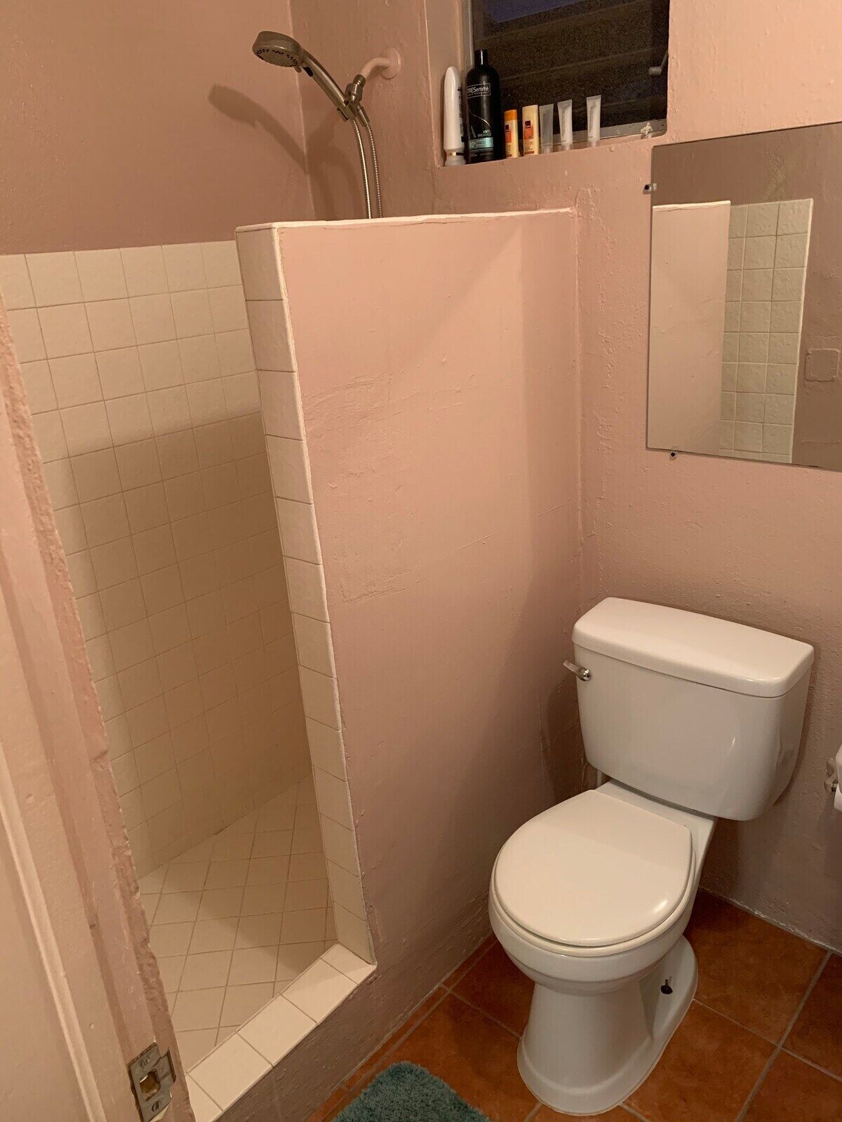 Une salle de bain avec des toilettes blanches, un espace douche et une petite fenêtre au-dessus du lavabo.