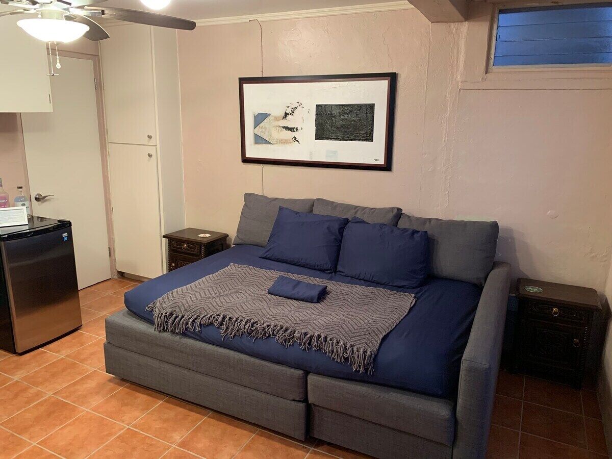 A bedroom with a bed, a small refrigerator, a nightstand, and a framed picture on the wall.
