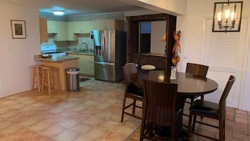 Uma sala de jantar com uma mesa redonda e cadeiras, uma cozinha ao fundo e uma lixeira.