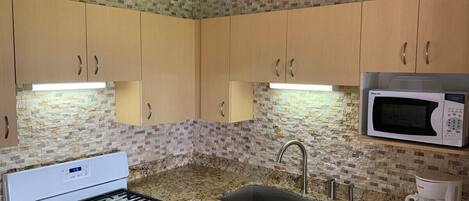 A compact kitchen with a gas stove, a microwave, a coffee maker, and a sink.