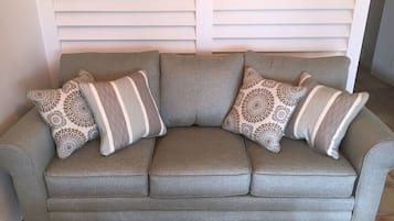 Ein graues Sofa mit gemusterten Kissen in einem Raum mit weißen Jalousien.