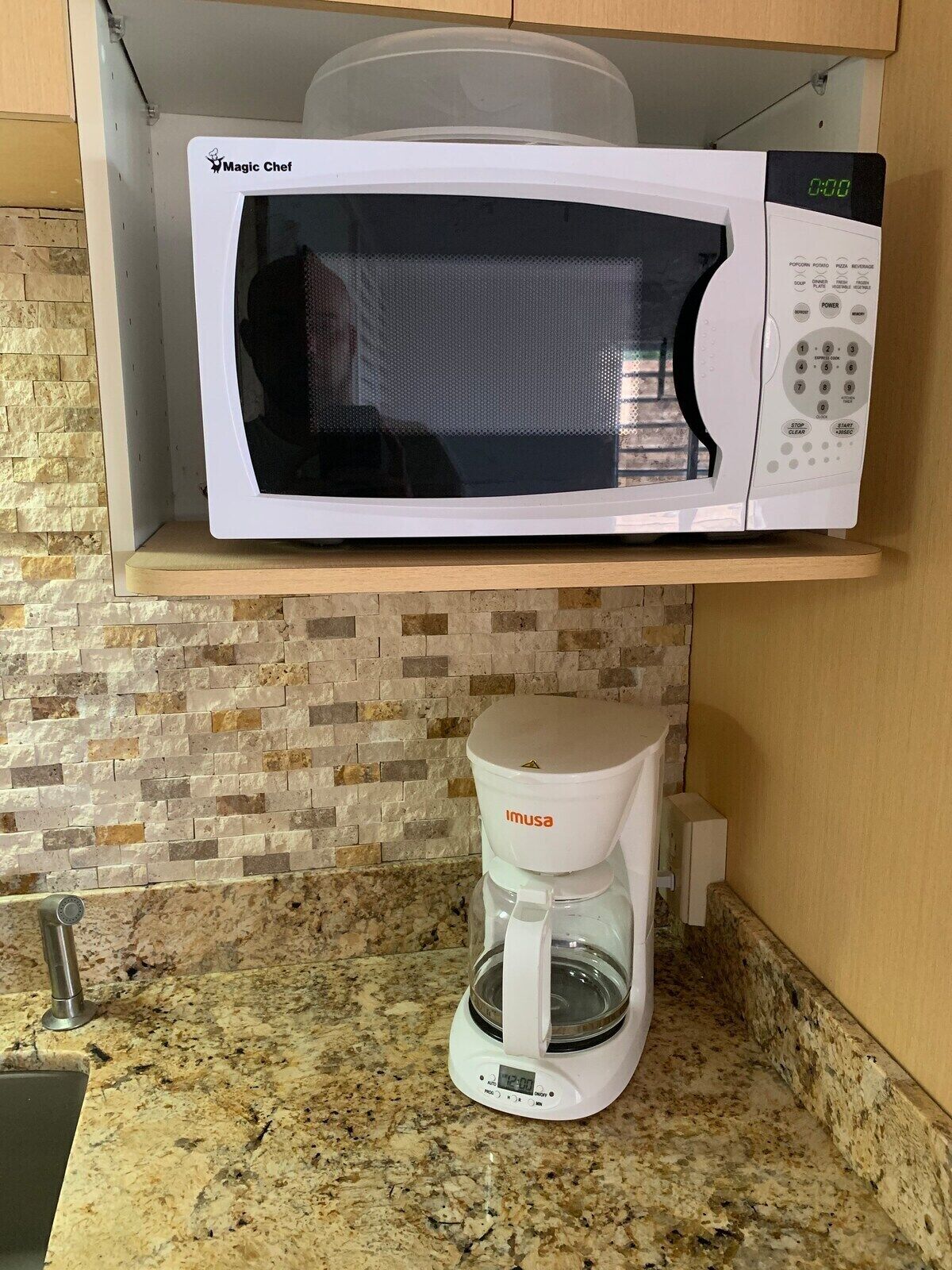 Una cocina con un microondas blanco Magic Chef en un estante, una cafetera Imusa blanca sobre la encimera y una encimera de granito.
