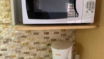 Una cocina con un microondas blanco Magic Chef en un estante, una cafetera Imusa blanca sobre la encimera y una encimera de granito.