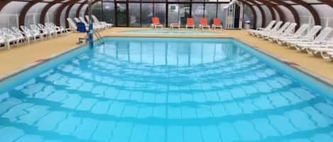 Una piscina interior con vista despejada al área de la piscina, rodeada de sillones de descanso y un techo cubierto.