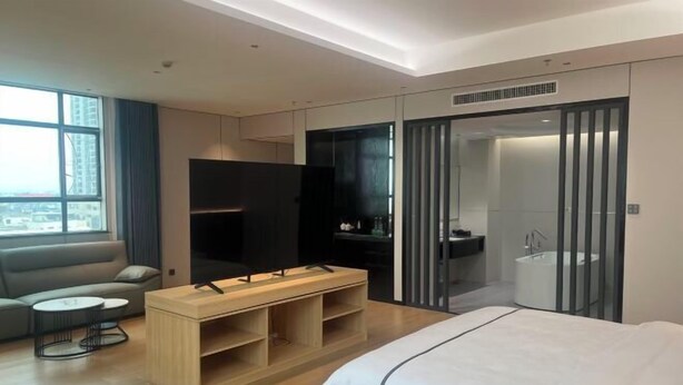 A modern hotel room with a large bed, a TV, a sofa, a small table, and a walk-in closet. - Jewel Business Hotel (Kaiping)