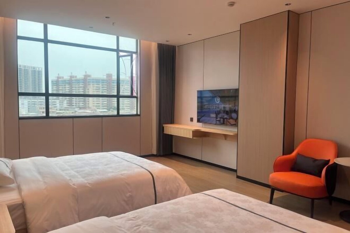 A modern hotel room with two beds, a TV, a desk, and a view of high-rise buildings.